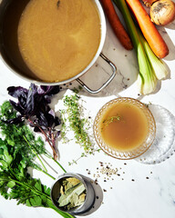 Vegetable stock in glass bowl. Ingredients of stock on the background. Top view