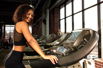 Obraz na płótnie Canvas African American woman smiling and running on a treadmill in the gym.