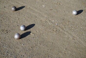 Silberne Boulekugeln auf feuchtem braunen Erdboden im Park bei Sonne am Nachmittag im Winter