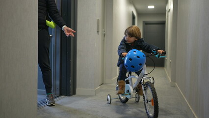 Mother and child leaving apartment. Little boy going out with bicycle standing at corridor by...