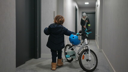 Mother and child leaving apartment. Little boy going out with bicycle standing at corridor by elevator door © Marco