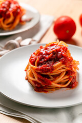 Vertical view of two spaghetti nests with tomato sauce over a wooden table, with a fork, kitchen towel, tomatoes and garlic