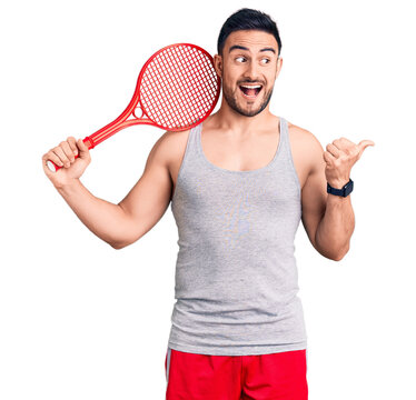 Young handsome man holding tennis racket pointing thumb up to the side smiling happy with open mouth