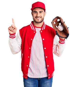 Young handsome man holding baseball gloves surprised with an idea or question pointing finger with happy face, number one