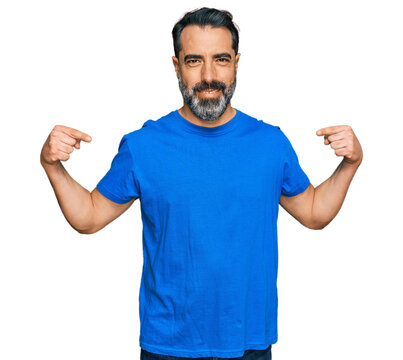 Middle aged man with beard wearing casual blue t shirt looking confident with smile on face, pointing oneself with fingers proud and happy.