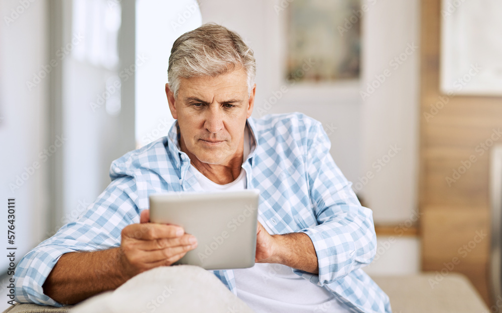 Poster Scrolling through websites. Shot of a mature man using his digital tablet while relaxing on his sofa at home.