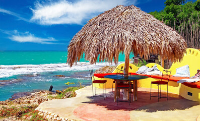 Empty colorful caribbean sun terrace, palm leaves umbrella, yellow seat bench, turquoise tropical...