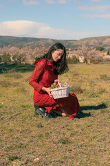 Woman wearing a red dress and holding a white basket with almond tree flowers