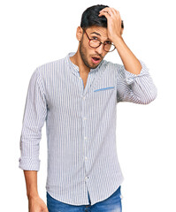 Young handsome man wearing casual clothes and glasses surprised with hand on head for mistake,...