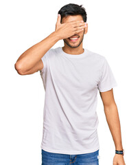 Young handsome man wearing casual white tshirt smiling and laughing with hand on face covering eyes for surprise. blind concept.