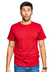 Obraz premium Young handsome man wearing casual red tshirt making fish face with lips, crazy and comical gesture. funny expression.