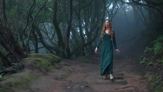 Beautiful woman in an elf costume is walking in a magic green enchanted forest.