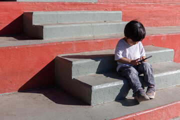 Fototapeta na wymiar Mexican kid playing with smart phone outdoors