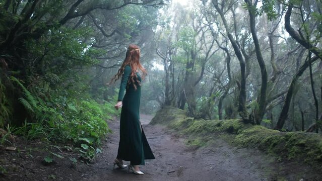Beautiful woman in an elf costume is walking in a magic green enchanted forest.