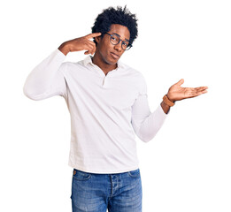 Handsome african american man with afro hair wearing casual clothes and glasses confused and annoyed with open palm showing copy space and pointing finger to forehead. think about it.