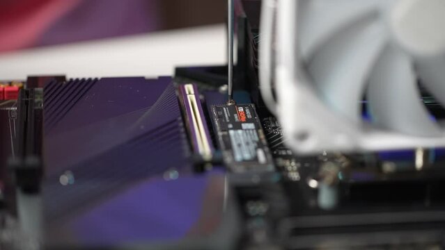 Close-up cropped shot of unrecognizable man screwing in bolts fixing new NVMe M.2 SSD stick onto gaming motherboard during custom PC build. Stages of upgrading or assembling desktop computer.