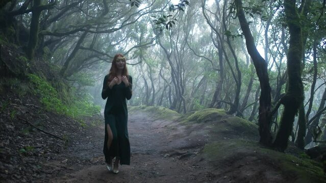 Beautiful woman in an elf costume is walking in a magic green enchanted forest.