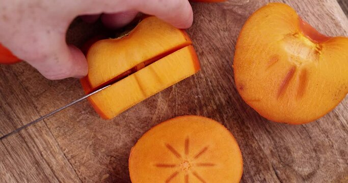 Half-ripe orange persimmon, fresh ripe persimmon cut into pieces on a cutting board with a sharp knife