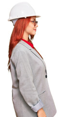 Young redhead woman wearing architect hardhat looking to side, relax profile pose with natural face with confident smile.