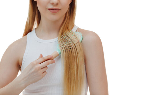 Good-looking blond woman combing hair with brush, holding comb and smiling happy at camera, standing over white background.