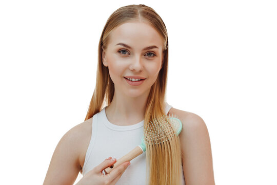 Young cute lady wrapped in towel, standing in front of mirror at bathroom and combing her hair with wooden brush after shower. Haircare cosmetics advert. Female beauty routine