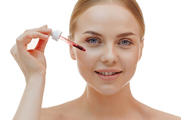 Happy smiling woman applies serum on her face, with pleasure. Blonde girl holding a dropper with skin care product for healthy and glowing skin tone, white background.