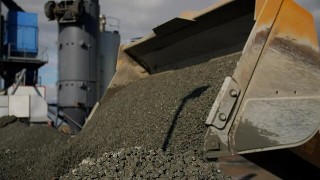 Excavator pours gravel onto pile from scoop against crushing tower at mining quarry closeup. Rock extracting technology