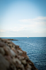 Mar mediterraneo en dénia, Valencia, España con velero navegando y rocas, con un cielo azul con nubes blancas.