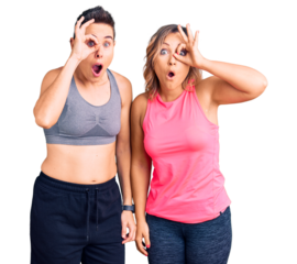 Couple of women wearing sportswear doing ok gesture shocked with surprised face, eye looking through fingers. unbelieving expression.