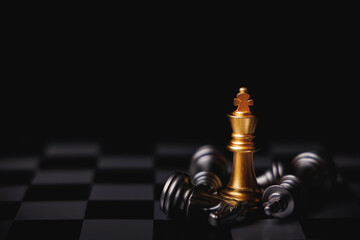 Gold king chess standing in center surround by fallen silver king chess, knight and other pieces in black background. Winner in business competition, marketing strategies and leadership concept.