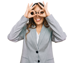 Young brunette woman wearing business clothes doing ok gesture like binoculars sticking tongue out, eyes looking through fingers. crazy expression.