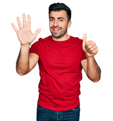 Naklejka premium Hispanic man with beard wearing casual red t shirt showing and pointing up with fingers number six while smiling confident and happy.