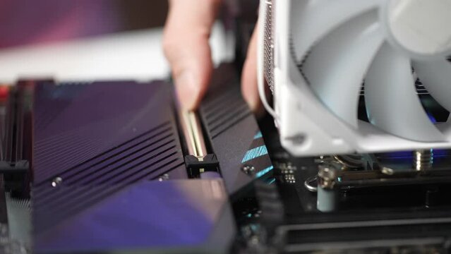 Closeup hands of unrecognizable man installing protective cover on NVMe M.2 SSD stick onto gaming motherboard during custom PC build. Stages of upgrading or assembling desktop computer.