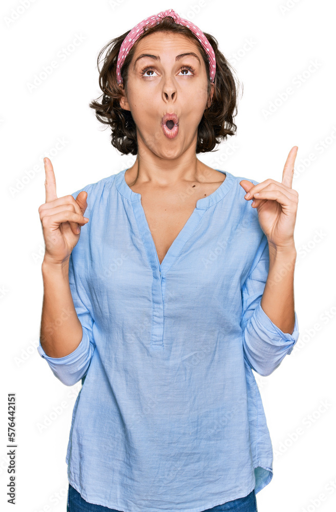 Poster young hispanic woman wearing casual clothes amazed and surprised looking up and pointing with finger