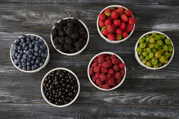 Fresh berries in six bowls on a wooden background. Fruit berry background.