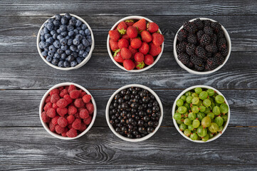 bowls with wild berries, wooden table background