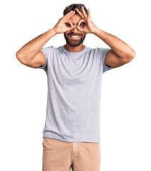 Young hispanic man wearing casual clothes doing ok gesture like binoculars sticking tongue out, eyes looking through fingers. crazy expression.