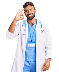 Young hispanic man wearing doctor uniform and stethoscope smiling positive doing ok sign with hand...