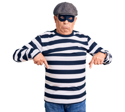 Senior handsome man wearing burglar mask and t-shirt pointing down looking sad and upset, indicating direction with fingers, unhappy and depressed.