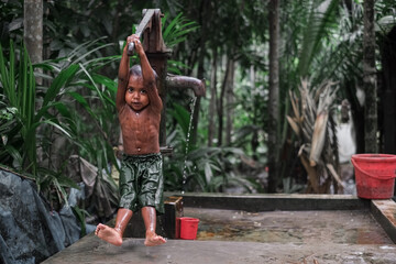 South asian little rural boy taking his bath from a tube well , self help is the best help concept 
