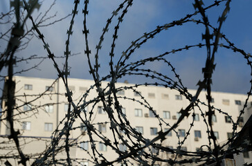 Barbed wire in the foreground, a house and a blue sky in the background in the sun.