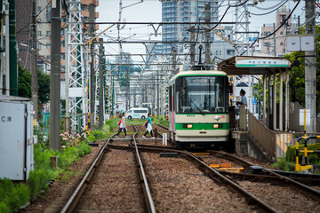 Tokyo Shitamachi trolly train (Toden) running in middle of city and two young asian girls walking across the tracks