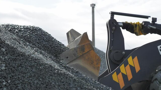 Bulldozer scoop takes gravel from heap at mining quarry closeup. Excavator operates with small rocks at construction site