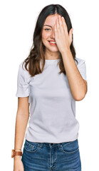 Fototapeta premium Young beautiful woman wearing casual white t shirt covering one eye with hand, confident smile on face and surprise emotion.