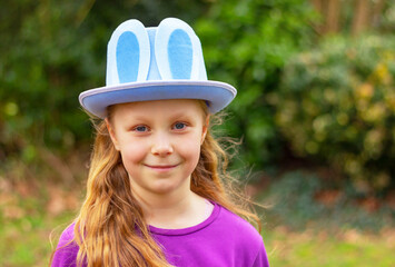 portrait of smiling child girl in blue Easter hat with rabbit ears on a natural background