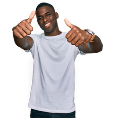 Young african american man wearing casual white t shirt approving doing positive gesture with hand, thumbs up smiling and happy for success. winner gesture.