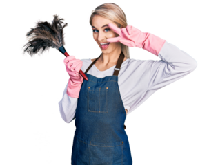 Beautiful young blonde woman wearing apron holding cleaning duster doing peace symbol with fingers over face, smiling cheerful showing victory