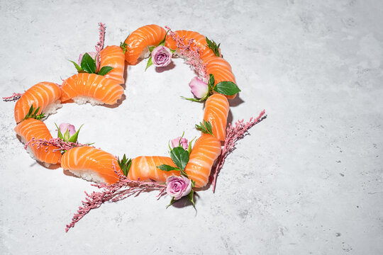 Sushi heart with flowers on grey background. Love sushi. Salmon nigiri with blooming roses. Women's day, Valentines day and spring celebration. Romantic dinner date. Creative Japanese set. Copy space