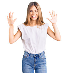 Fototapeta na wymiar Beautiful caucasian woman with blonde hair wearing casual white tshirt showing and pointing up with fingers number ten while smiling confident and happy.