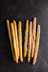 Italian grissini bread sticks with sesame seeds on black table. Top view.
